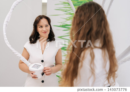 Smiling friendly doctor preparing client for hardware cosmetology procedure, utilizing advanced skin lifting technology for facial and body aesthetic medicine treatments. Concept of healthy lifestyle. Smiling friendly doctor preparing client for hardware cosmetology procedure, utilizing advanced skin lifting technology for facial and body aesthetic medicine treatments. Concept of healthy lifestyle. 143073776