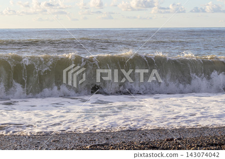 A powerful sea wave churning and breaking into white foam on a pebble beach. Nature A powerful sea wave churning and breaking into white foam on a pebble beach. Nature 143074042