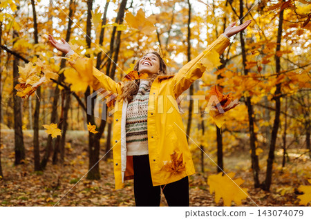 Happy woman in a yellow raincoat has fun in the autumn forest. Day in nature. Nature, travel concept Happy woman in a yellow raincoat has fun in the autumn forest. Day in nature. Nature, travel concept 143074079