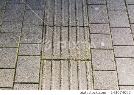 High angle view of tactile paving tiles with linear ridges on a concrete block sidewalk. Texture High angle view of tactile paving tiles with linear ridges on a concrete block sidewalk. Texture 143074092