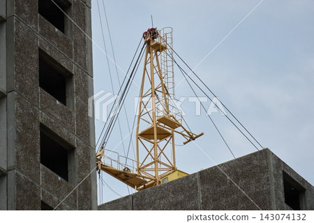 Wide view of tower crane mechanisms working near panel house structure under daylight Wide view of tower crane mechanisms working near panel house structure under daylight 143074132