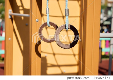 Detailed close up shot of outdoor plywood gymnastic fitness rings hanging on a blue rope at a modern wooden children playground structure Detailed close up shot of outdoor plywood gymnastic fitness rings hanging on a blue rope at a modern wooden children playground structure 143074134