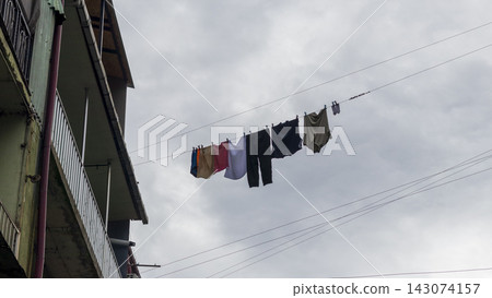 Low angle view of clothes and laundry hanging to dry on a line outside an apartment building. City Low angle view of clothes and laundry hanging to dry on a line outside an apartment building. City 143074157