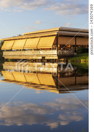 Vibrant golden reflection of a waterfront restaurant with yellow awnings on a calm lake. Outdoors Vibrant golden reflection of a waterfront restaurant with yellow awnings on a calm lake. Outdoors 143074169