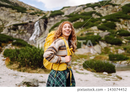 A person is walking up a rocky trail with a large backpack. A waterfall is visible in the background A person is walking up a rocky trail with a large backpack. A waterfall is visible in the background 143074452