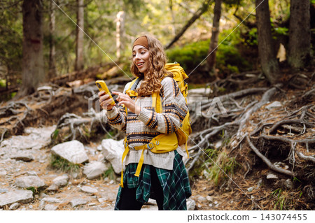 A person stands on a rocky trail in a forest. They look at their phone while wearing a backpack. A person stands on a rocky trail in a forest. They look at their phone while wearing a backpack. 143074455