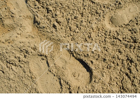 top-down close-up shot of a patch of damp yellow sand with a light human footprint compression 143074494