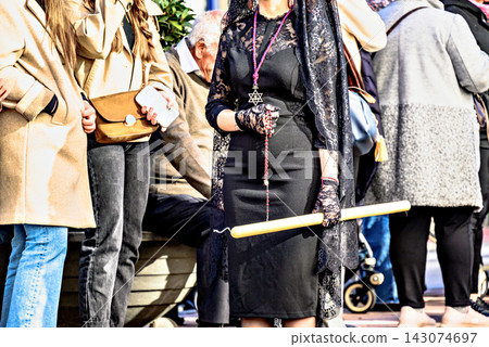 A woman dressed in traditional manola attire (with a black mantilla), holding a rosary and a large candle during a Holy Week procession in Granada, Andalusia, Spain. A woman dressed in traditional manola attire (with a black mantilla), holding a rosary and a large candle during a Holy Week procession in Granada, Andalusia, Spain. 143074697