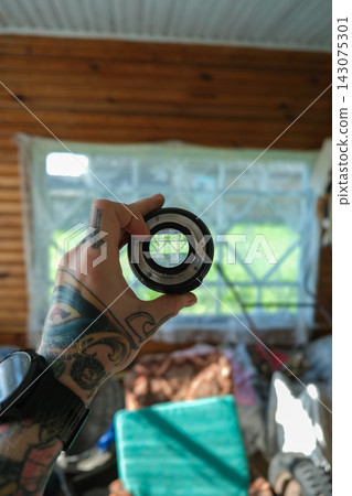 Tattooed hand holds camera mount by sunlit cabin window in Belarus Tattooed hand holds camera mount by sunlit cabin window in Belarus 143075301