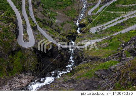 Aerial view of mountain road with hairpin turns crossing river gorge, Norway 143075380