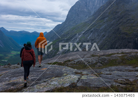 Trail runners on mountain plateau with steep rock face, Norway valley vista Trail runners on mountain plateau with steep rock face, Norway valley vista 143075403