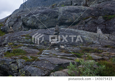 Rock cairn stacked on dark granite boulders, Norway mountain terrain 143075415