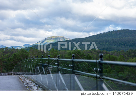 Observation deck railing overlooking forested valley with mountain backdrop, Norway Observation deck railing overlooking forested valley with mountain backdrop, Norway 143075429