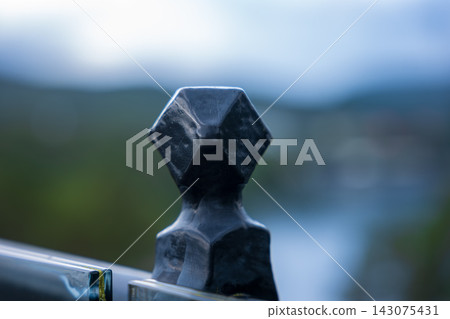 Close-up of hexagonal stone finial on metal railing, blurred mountain landscape, Norway Close-up of hexagonal stone finial on metal railing, blurred mountain landscape, Norway 143075431