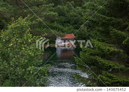 Boathouse with red metal roof on forested waterway, Norway Boathouse with red metal roof on forested waterway, Norway 143075452