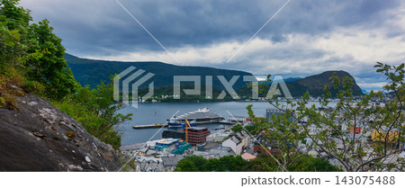 Cruise ship docked at harbor with fjord mountains and coastal settlement, Norway 143075488