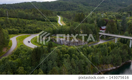 Aerial view of winding mountain road with concrete bridge viaduct over forested valley, Straumen Norway 143075616