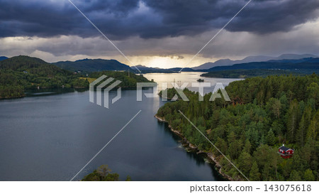 Aerial view of Straumen lake with coniferous forest, mountains and red cabin, Norway 143075618