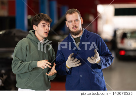 Guy discusses further repairs to his car with car mechanic at car service center 143078525