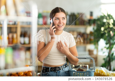 Young woman choosing groceries while talking on phone Young woman choosing groceries while talking on phone 143078526