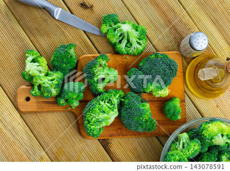 Florets of fresh raw broccoli on wooden cutting board with oil and spices Florets of fresh raw broccoli on wooden cutting board with oil and spices 143078591
