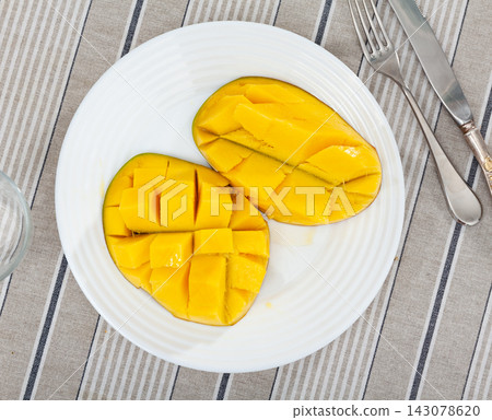 Two halves of ripe yellow mango cut into cubes lie on white round plate Two halves of ripe yellow mango cut into cubes lie on white round plate 143078620
