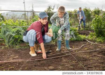 Woman planting seeds boy watering beds Woman planting seeds boy watering beds 143078638