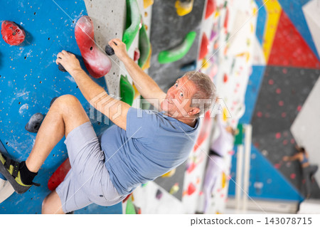 Alpinist practicing indoor rock climbing on artificial boulder without safety belts 143078715