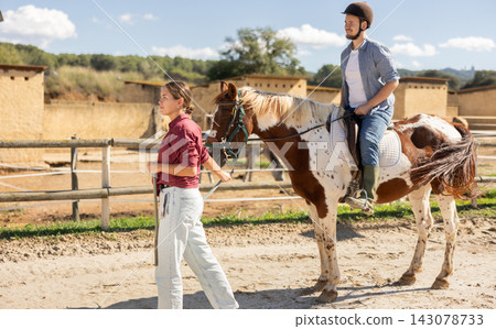 Young woman leading horse with man riding 143078733