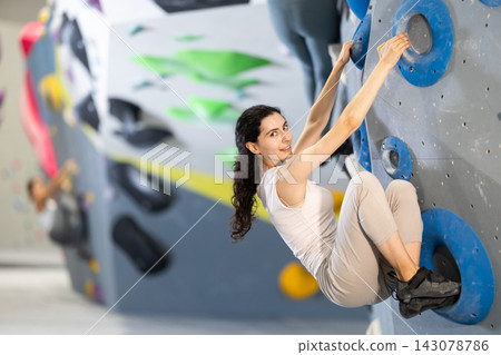 Motivated young girl climbing without ropes and harnesses on artificial bouldering wall in fitness center Motivated young girl climbing without ropes and harnesses on artificial bouldering wall in fitness center 143078786