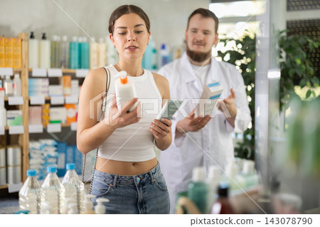Girl chooses skin cream in modern pharmacy. Male pharmacist helps with choosing medicine Girl chooses skin cream in modern pharmacy. Male pharmacist helps with choosing medicine 143078790