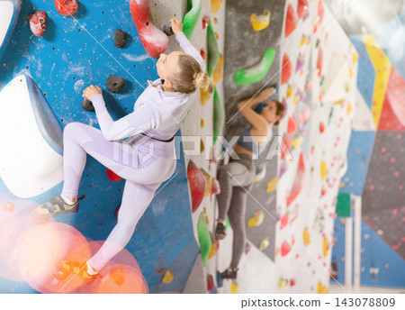 Young female alpinist practicing indoor rock-climbing on artificial boulder without safety belts Young female alpinist practicing indoor rock-climbing on artificial boulder without safety belts 143078809