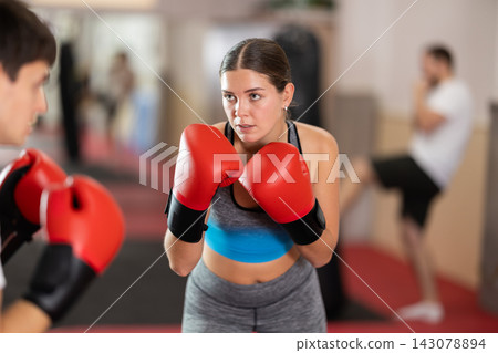Girl punches, tries to defeat guy opponent during training fight in ring. Girl punches, tries to defeat guy opponent during training fight in ring. 143078894