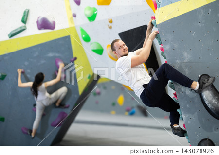 Man climbing a tall, indoor, man made rock climbing wall Man climbing a tall, indoor, man made rock climbing wall 143078926