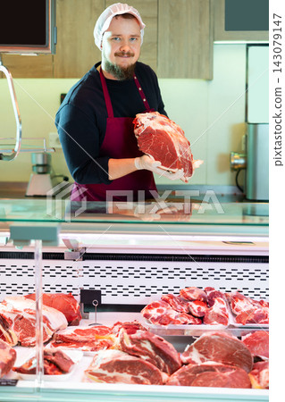 Male butcher putting raw meat on supermarket display Male butcher putting raw meat on supermarket display 143079147