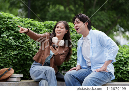 Asian friends pointing and looking away while resting outdoors on campus 143079499
