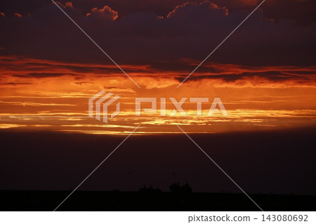 A dramatic sunset paints the gaps between dark clouds in a vibrant orange hue. A dramatic sunset paints the gaps between dark clouds in a vibrant orange hue. 143080692