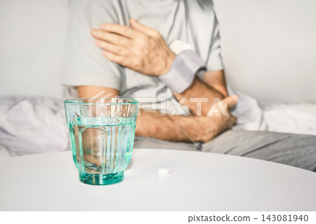Mature man checking blood pressure at home, medication and glass of water nearby Mature man checking blood pressure at home, medication and glass of water nearby 143081940