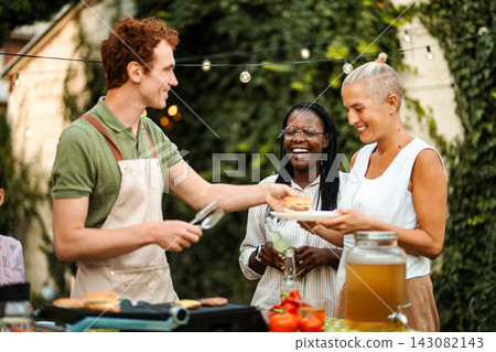 Man serving burgers to friends at outdoor BBQ party 143082143