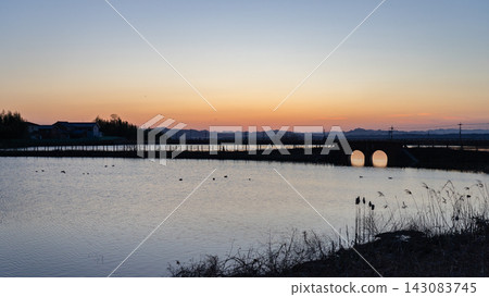 A tranquil rural landscape with a pond and bridge at dusk, and distant mountain ranges in view. A tranquil rural landscape with a pond and bridge at dusk, and distant mountain ranges in view. 143083745