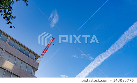 湛藍的天空,一棟建築物旁矗立著一台紅色的建築起重機。 湛藍的天空,一棟建築物旁矗立著一台紅色的建築起重機。 143083776