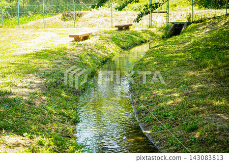 寧靜的景色,一條狹窄的水道穿過綠樹成蔭的公園,公園裡擺放著木製長椅。 寧靜的景色,一條狹窄的水道穿過綠樹成蔭的公園,公園裡擺放著木製長椅。 143083813