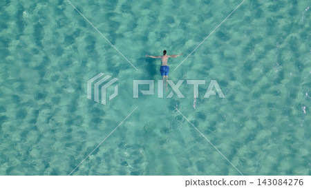 Aerial top down view of man swimming on his back in crystal clear turquoise sea water at Elafonisi beach in paradise island Crete Greece Aerial top down view of man swimming on his back in crystal clear turquoise sea water at Elafonisi beach in paradise island Crete Greece 143084276