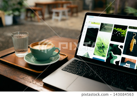Remote work lifestyle, laptop screen showing photos with a cup of hot coffee on rustic wooden table. 143084563