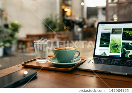 Content creator working on laptop in cafe. Browsing inspiration photos with coffee and smartphone on desk. Content creator working on laptop in cafe. Browsing inspiration photos with coffee and smartphone on desk. 143084565