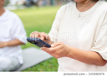 Close Up of Senior Woman Using Smartphone Outdoor Park Yoga. 143086974