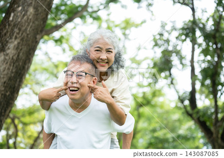 Elderly Asian Couple Piggyback Ride With Playful Face Pinching And Big Smiles. Elderly Asian Couple Piggyback Ride With Playful Face Pinching And Big Smiles. 143087085