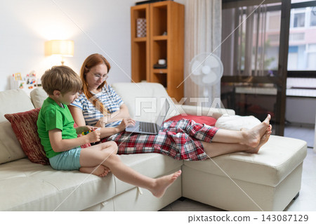 Mother and son work on tasks together in cozy living room during afternoon at home Mother and son work on tasks together in cozy living room during afternoon at home 143087129
