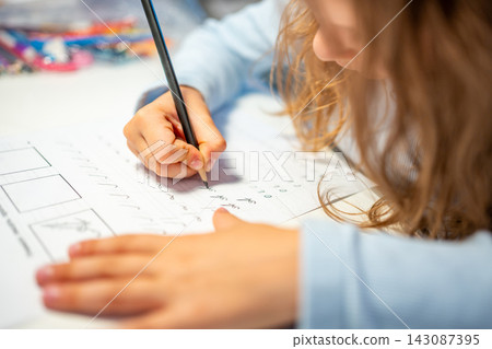 First grade girl practices handwriting with pencil in school workbook. Child learns to write letters during early education with selective focus and shallow depth of field 143087395