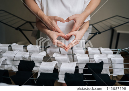 Loving couple forming heart gesture with hands over drying rack full of newly washed white and black socks, symbolizing shared domestic chores, teamwork, love, partnership in daily life, close-up. Loving couple forming heart gesture with hands over drying rack full of newly washed white and black socks, symbolizing shared domestic chores, teamwork, love, partnership in daily life, close-up. 143087396
